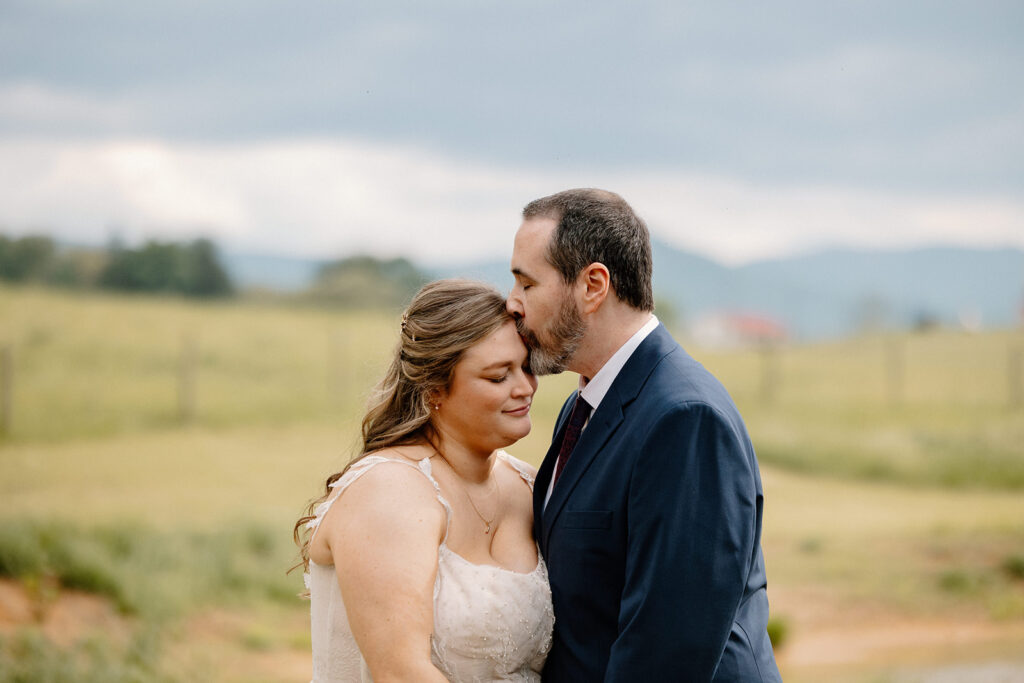 A groom kisses the top of the forehead of his bride on their intimate wedding day.