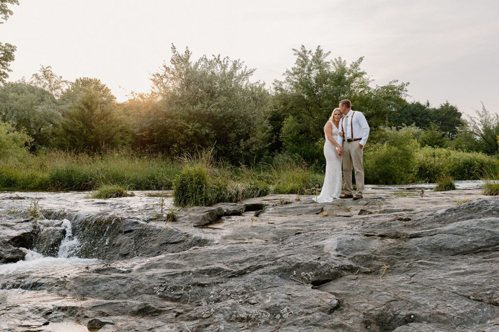A bride and groom stand on some rocks at a waterfall in Virginia on their elopement day.