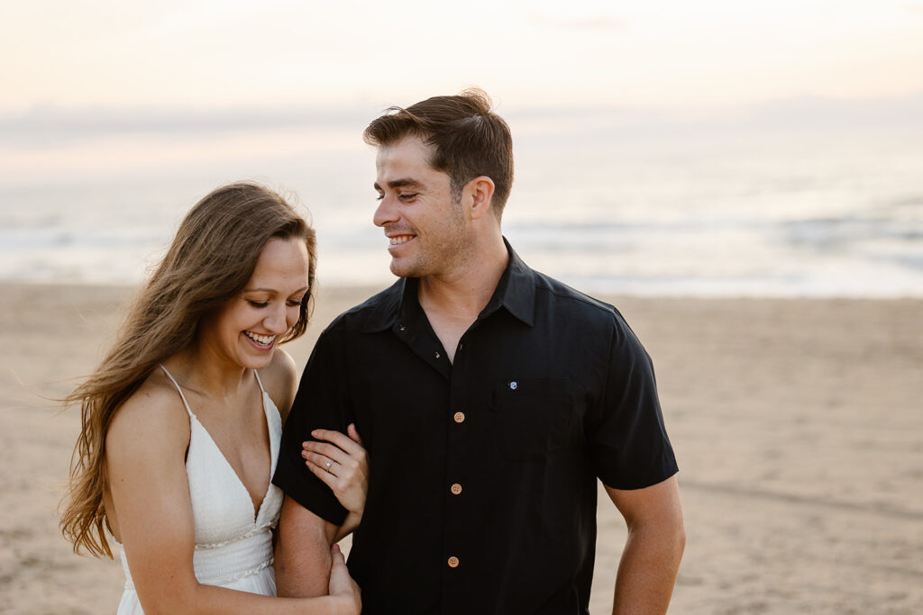 A bride holds her grooms arm at the beach during their sunrise elopement day