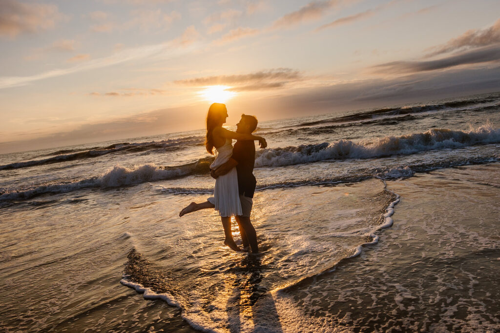 A groom lifts his bride at sunrise at a beach in Virginia. 