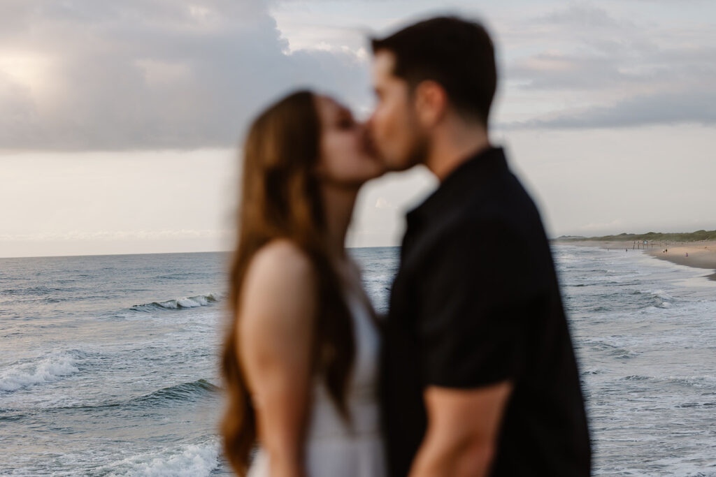 An out of focus bride and groom kiss in front of an unfocus view of the ocean, on their elopement day 