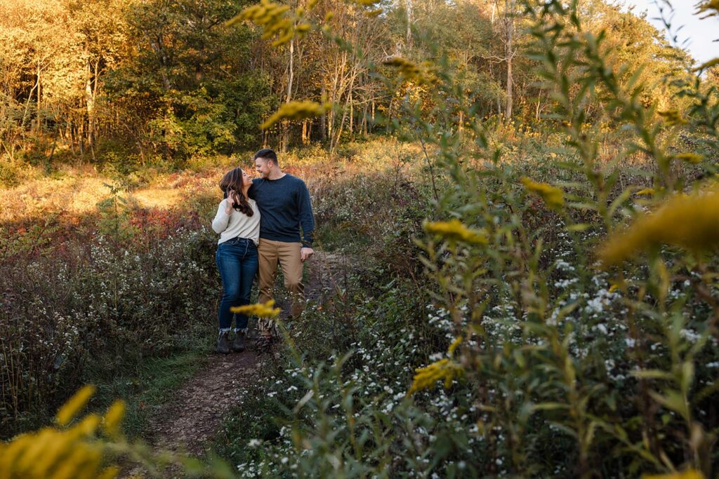 A bride and groom walk through a field of goldenrod and fall wildflowers on their elopement day. Shenandoah Fall Colors
