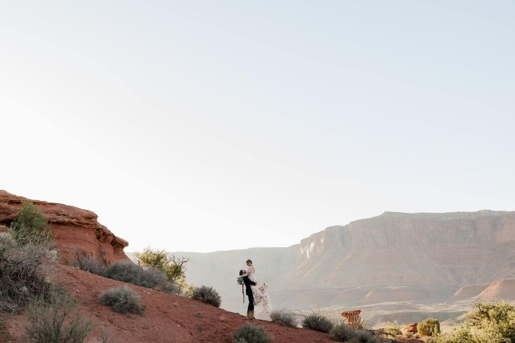 A groom lifts up his bride in Castle Valley inn Moab during their sunset elopement ceremony at Hauer Ranch
