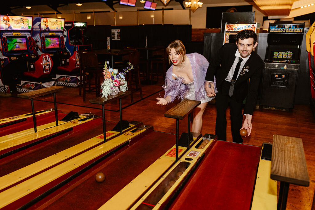 A bride and groom play skee ball during their elopement reception at a vintage arcade