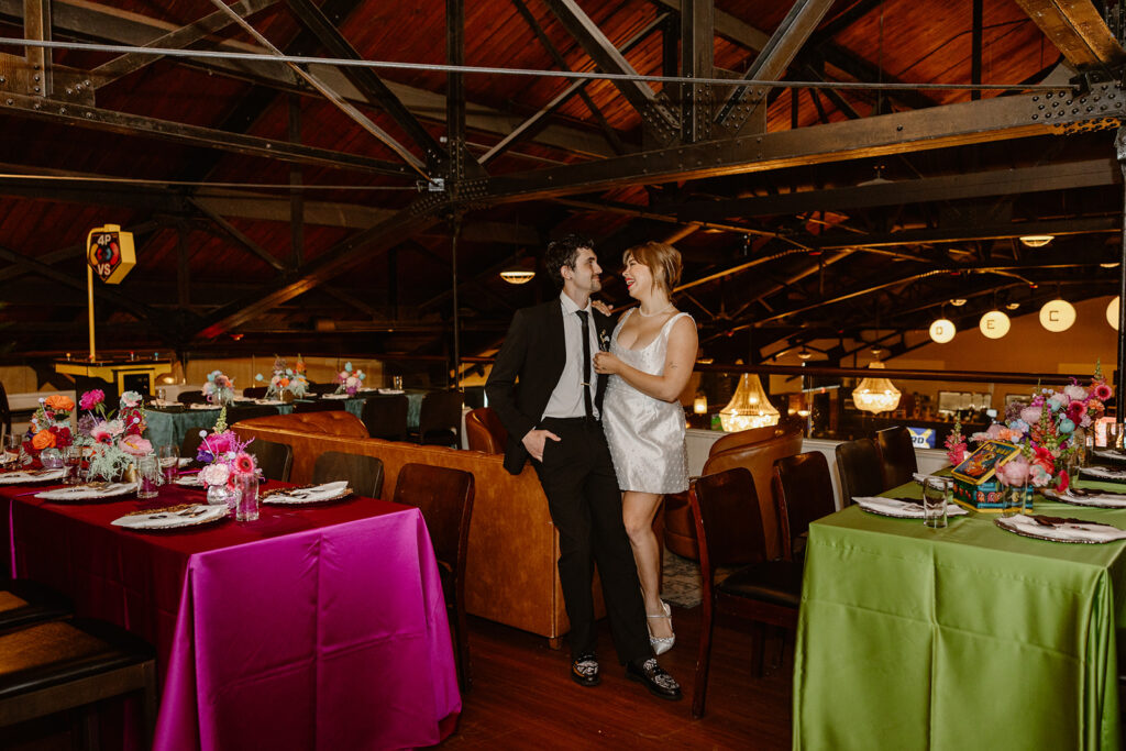 A bride and groom snuggle against a couch in the middle of the reception. 