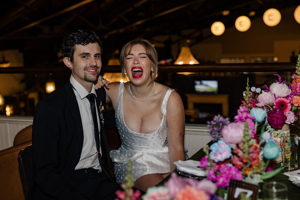 A bride caught laughing while sitting at a table at her reception