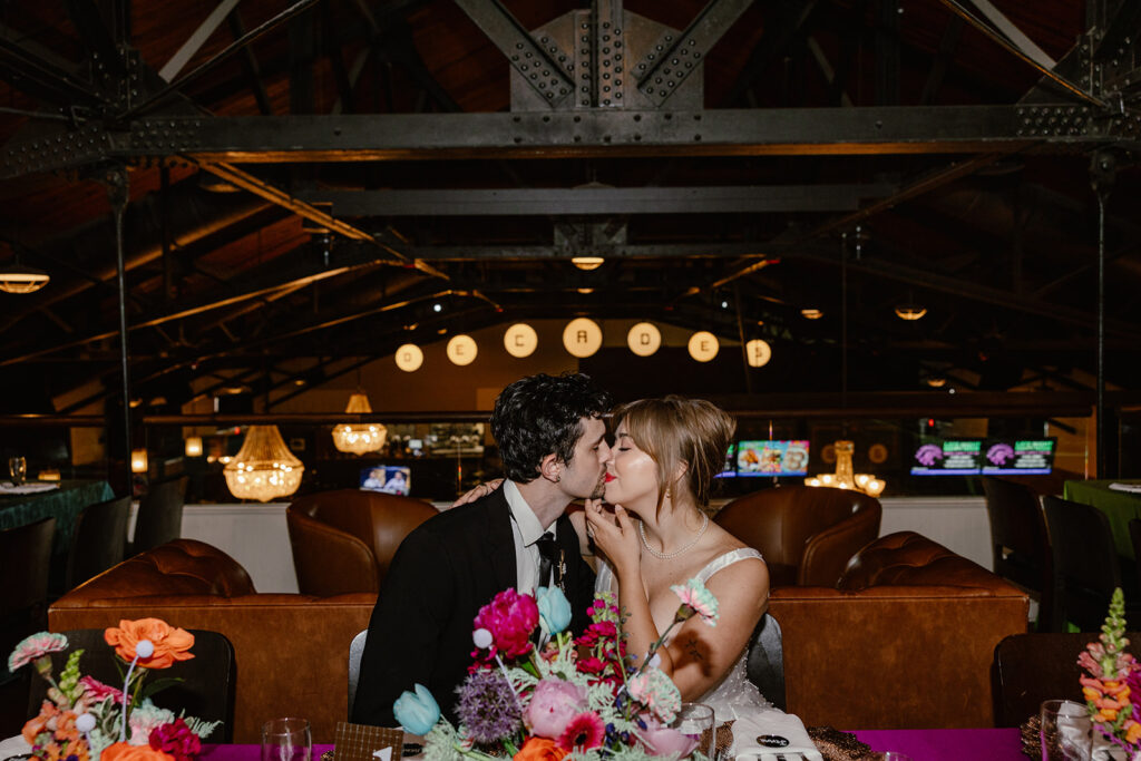 A couple kisses during their non traditional wedding reception at a vintage arcade