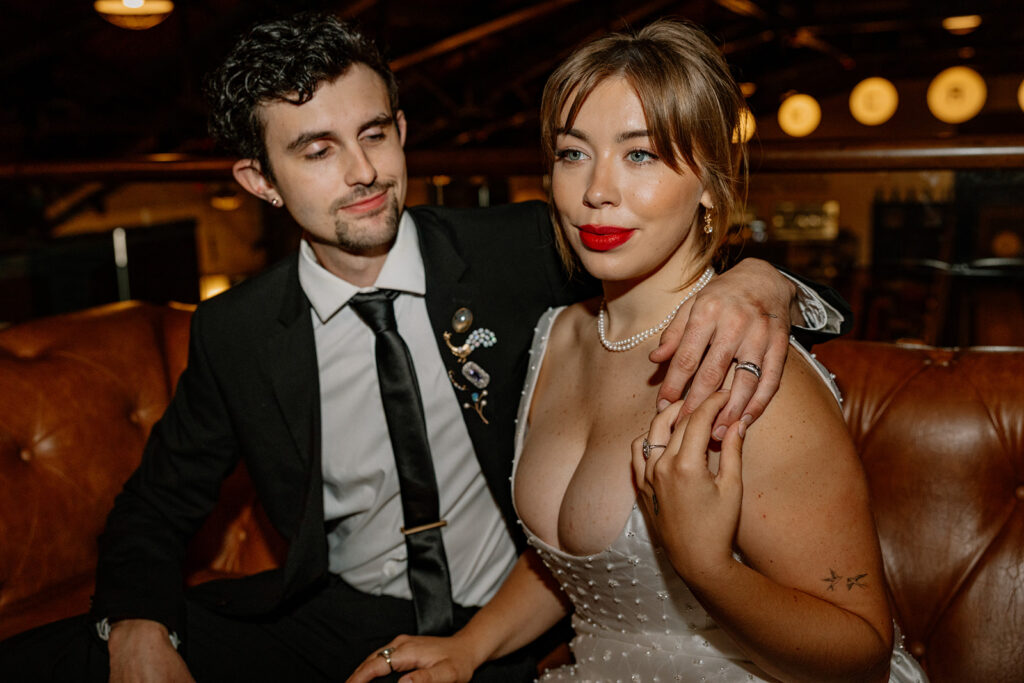 A groom has his arm around his bride at they sit on a leather couch during tier elopement reception