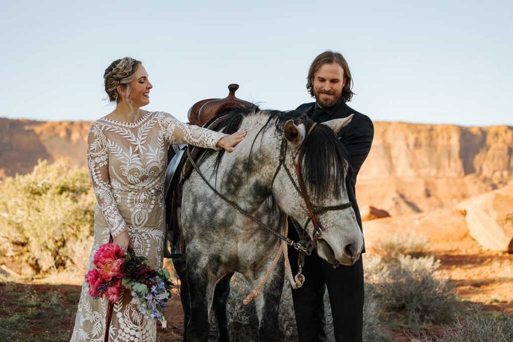 A bride and groom pet a horse before their sunset ride in Castle Valley in Moab