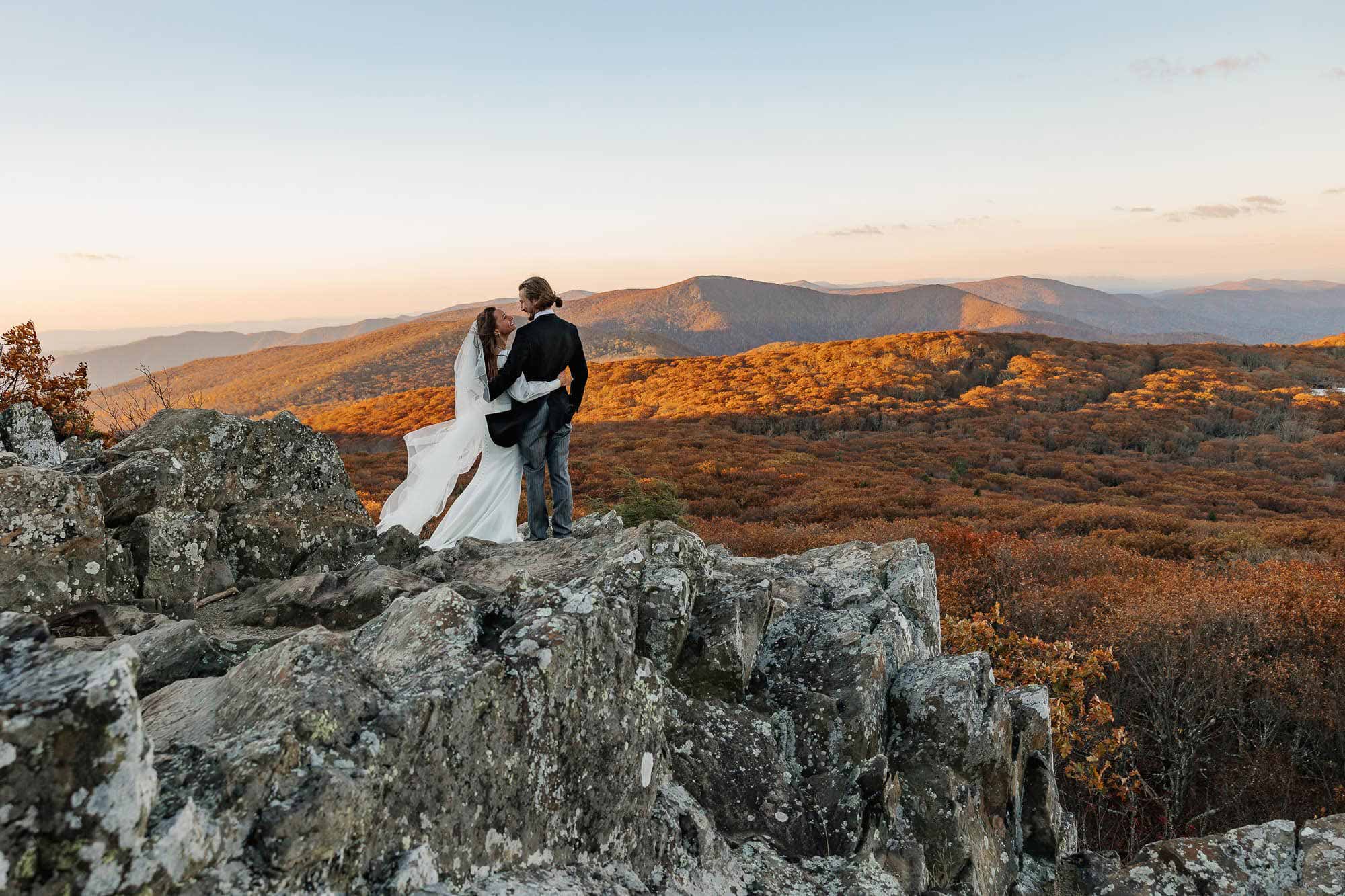 A couple stands and admires the peak fall colors at Shenandoah National Park during their sunrise elopement