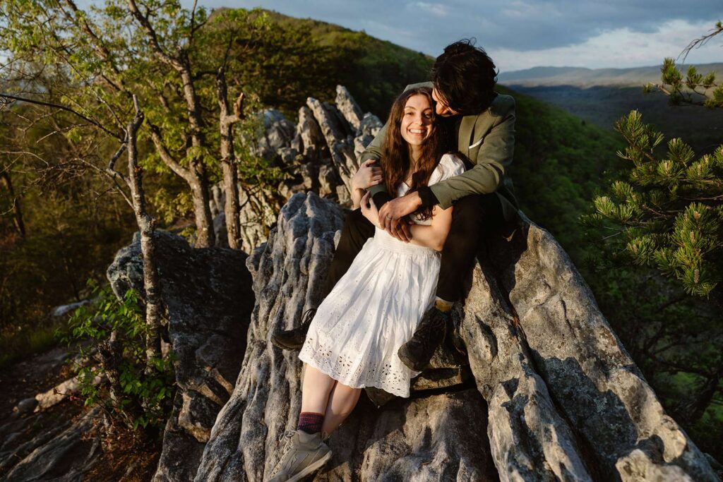 A bride and groom snuggle on a rock together at Buzzard Rock during their sunrise elopement