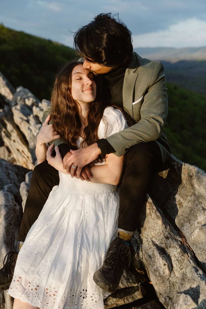 A bride and groom snuggle on a rock together at Buzzard Rock on their wedding day.