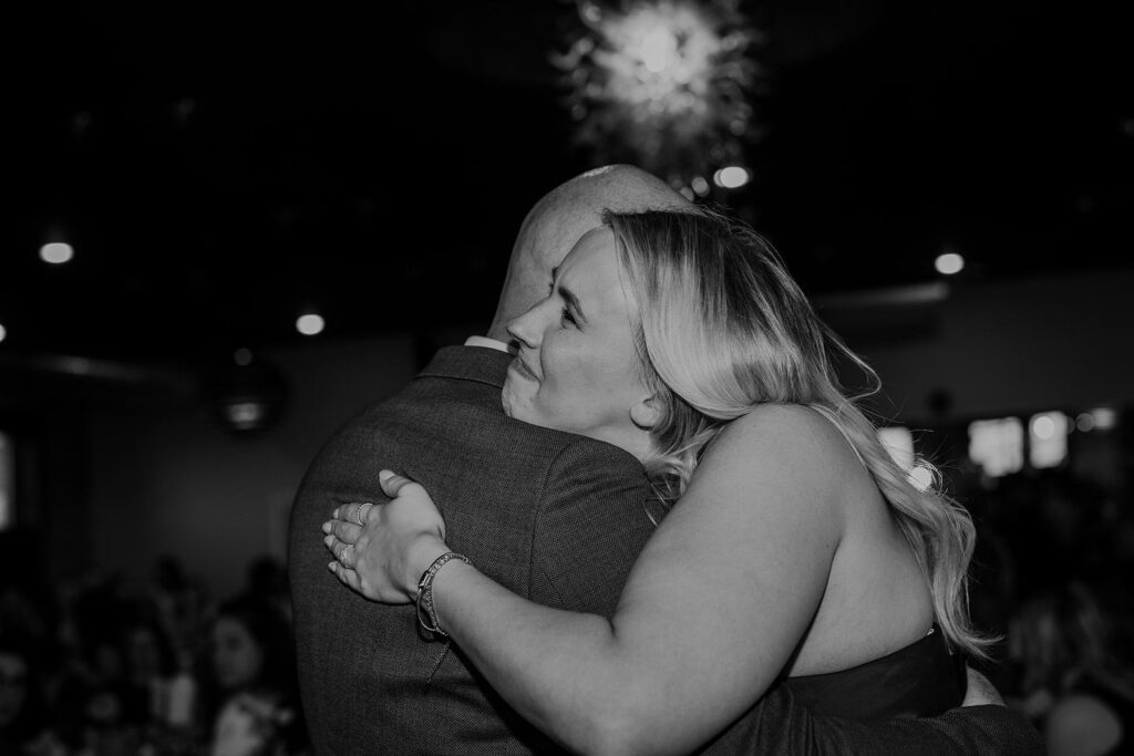 The grooms daughter hugs her dad sweetly as they dance during his wedding reception.