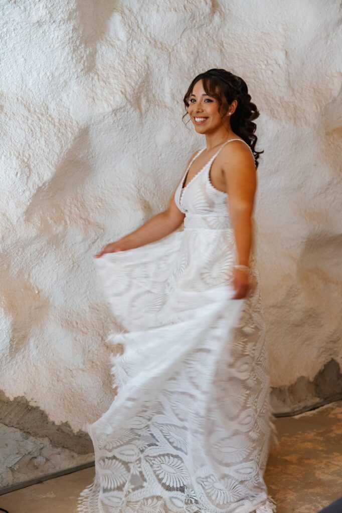 Bride twirling in her lace wedding dress inside a cave-style room with textured white walls.