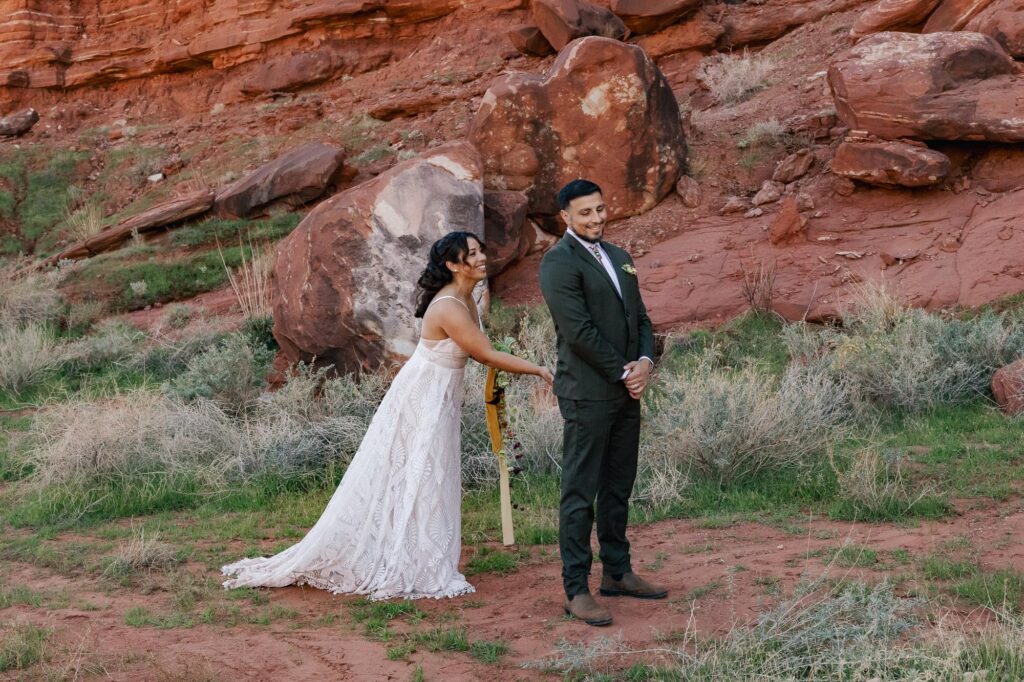 A bride squeezes the butt of her groom to signal him to turn around during the first look of their wedding day.