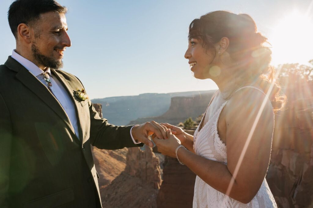 A bride puts on the grooms ring during their elopement ceremony at Marlboro Point in Utah. The sun is backlighting them.