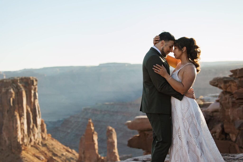 A bride and groom embrace with their foreheads touching in front of a desert canyon during their jeep adventure elopement in Marlboro Poit