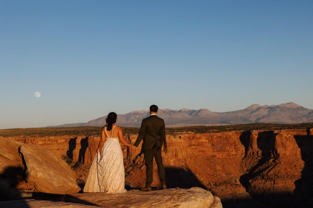 A bride and groom hold hands looking at the super moon rising.