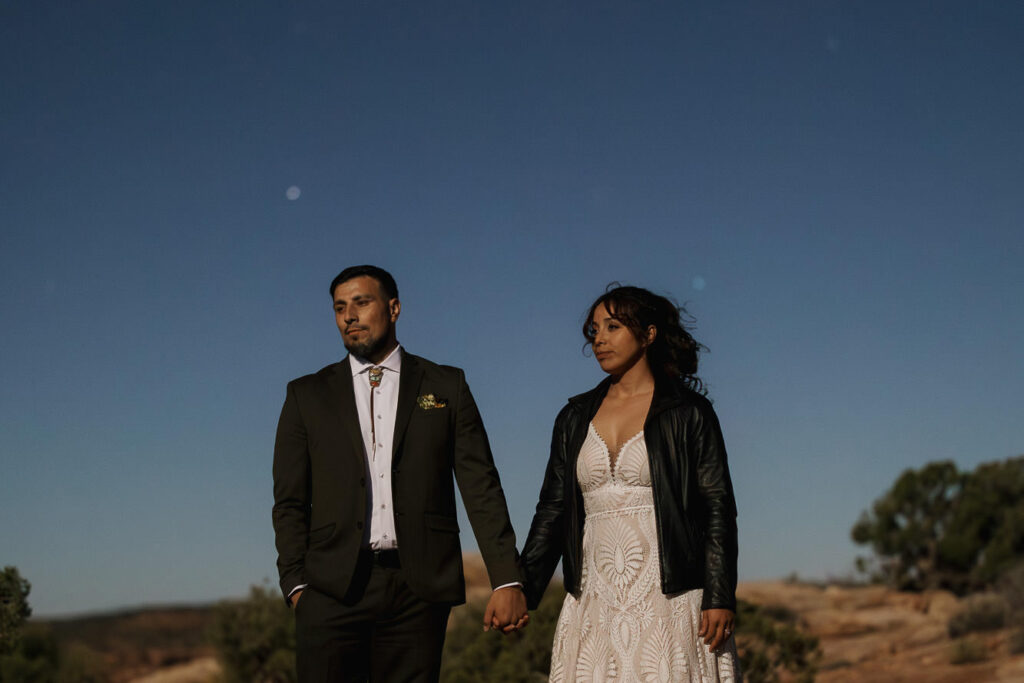 A birde and groom stand hand in hand looking off in the distance as the super moon lights their faces to the point it looks like dylight.