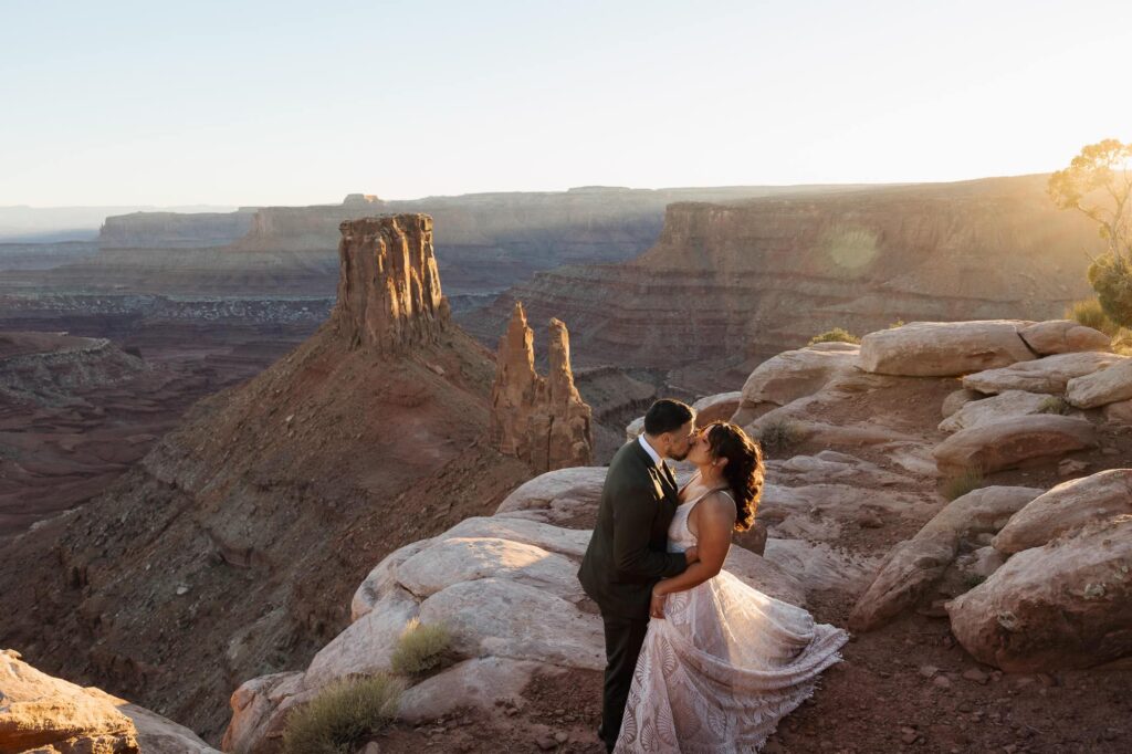 A bride and groom kiss in front of a setting sun in Utah.