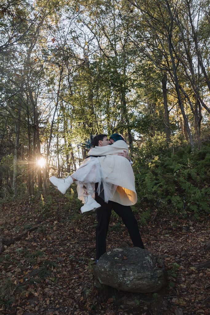 A groom picks up his bride and kisses her on their chilly sunrise elopement