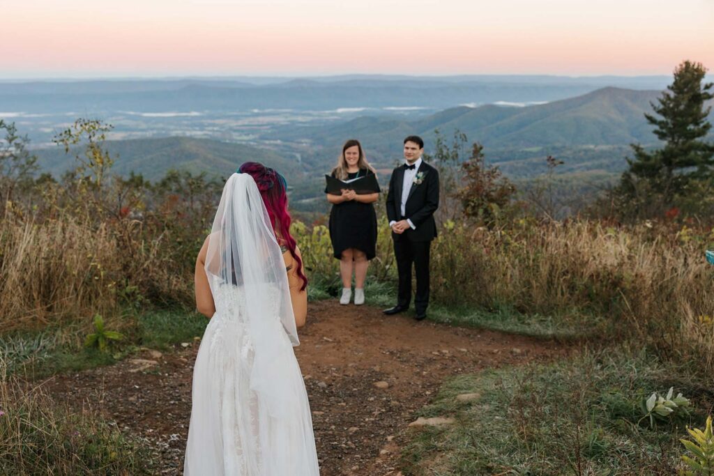 The back of a bride walking towards her groom and the officiant standing in front of the mountains in Shenandoah National Park