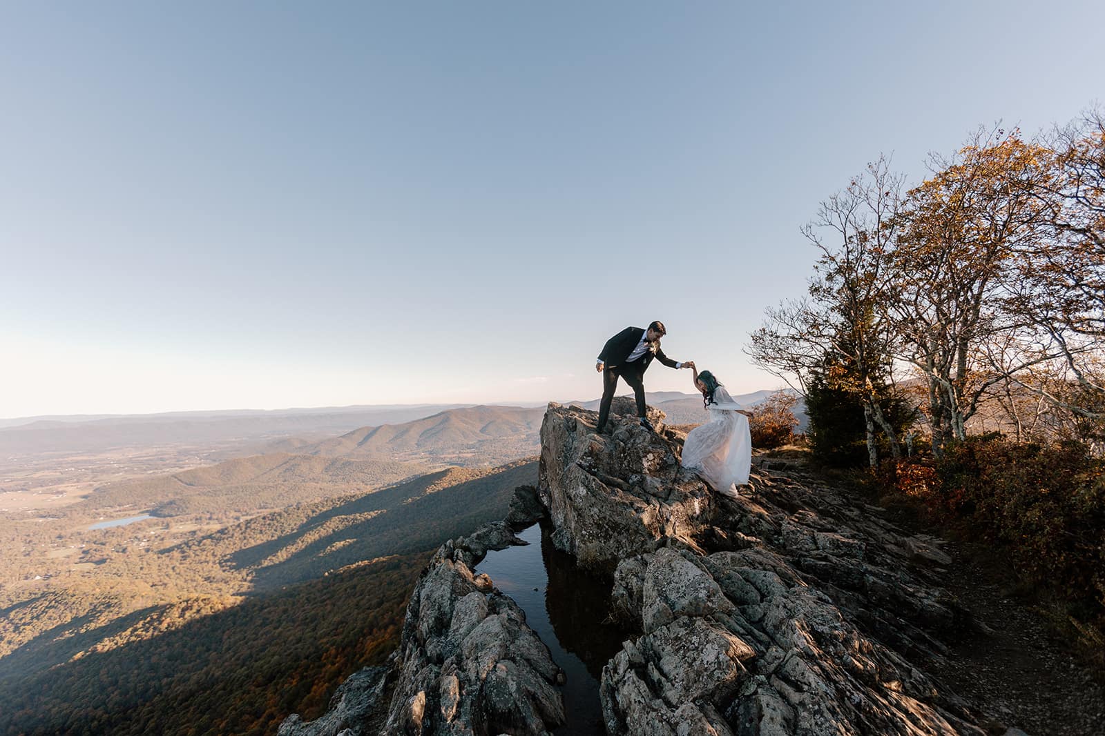 A groom lends a hand to his bride to help her up to the top of Little Stony Man during their Shenandoah Elopement