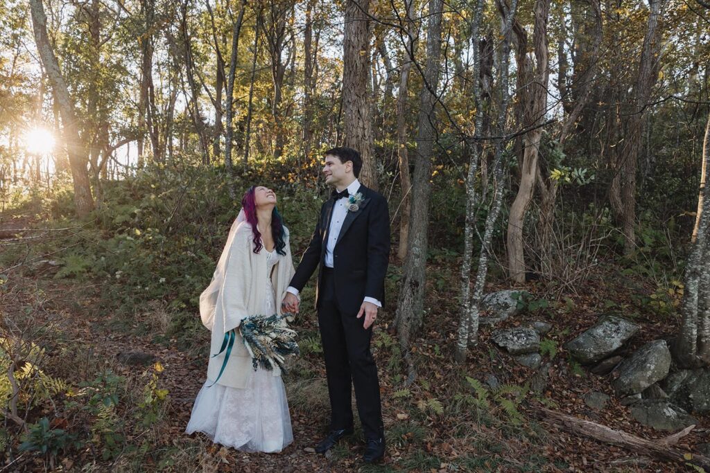 A bride is laughing hard at something the groom said during their elopement in Shenandoah. He is wearing a tux, and she is wearing a strapless gown with a white coat.