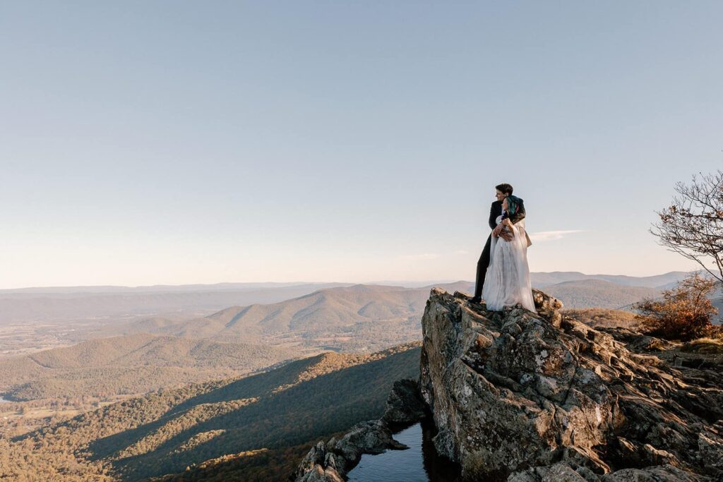 A bride and groom snuggle close while standing a top of Little Stony Man during their elopement. They are looking out enjoying the view