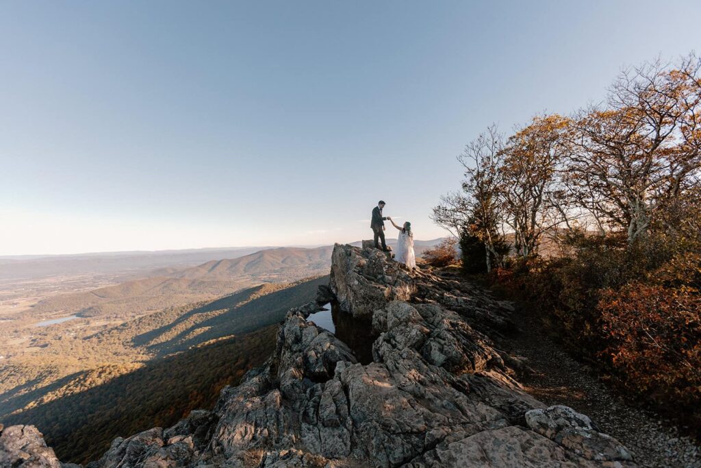 A bride holds the hand of her groom, and leads him down the top of Little Stony Man.