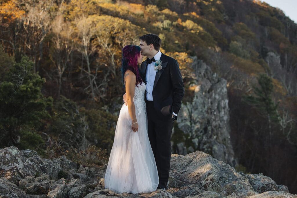 A groom kisses the forehead of his bride at Little Stony Man in Shenandoah during their adventure elopement