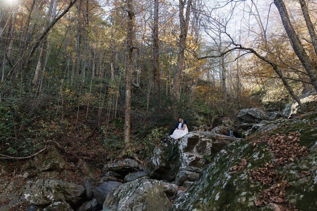 A bride and groom sit on some boulders on the Rose Rover Trail during a hike on their elopement day.