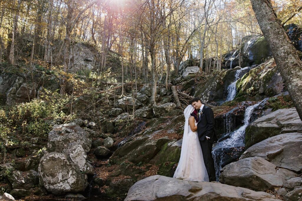 A bride and groom stand together at the base of Dark Hollow Falls in Shenandoah during their adventure elopement
