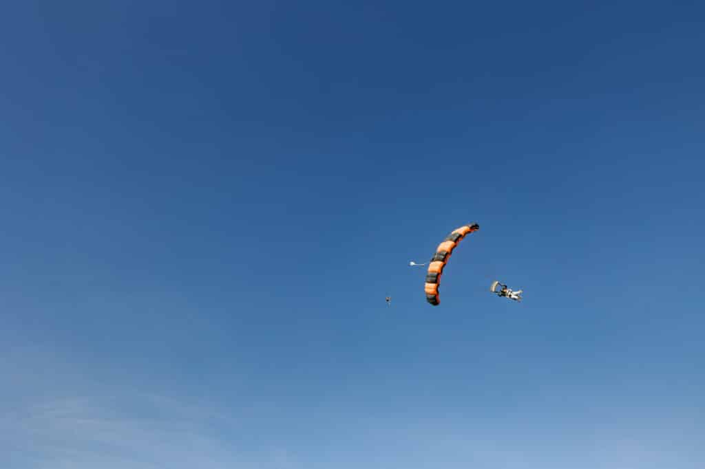 A bride seen in the blue sky skydiving on her wedding day. You can see the grooms parachute in the distance
