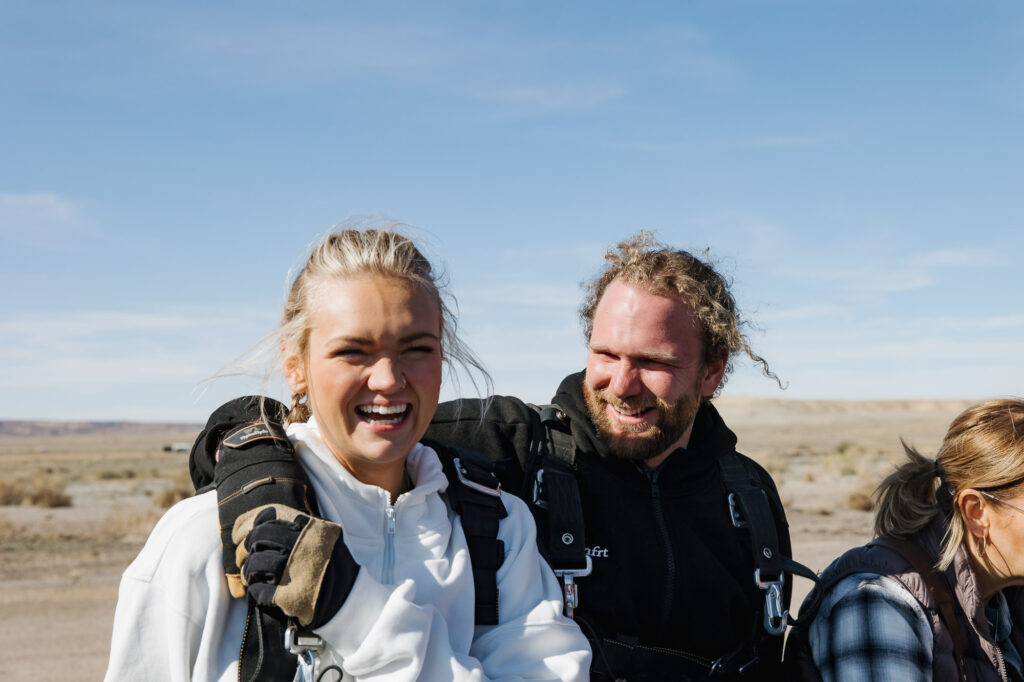 A groom has his arm around the bride while they smile from skydiving for the first time on their elopement day.