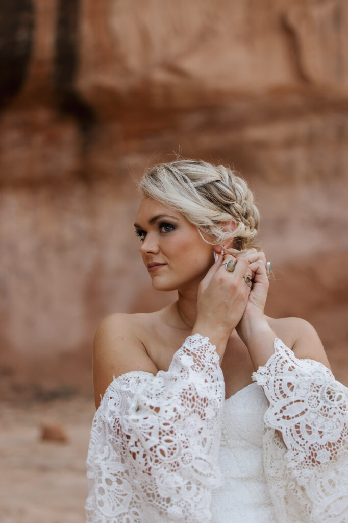 A bride puts in an earring as she gets ready for her adventure elopement in Moab. She is wearing a romantic Boho dress with lace sleeves