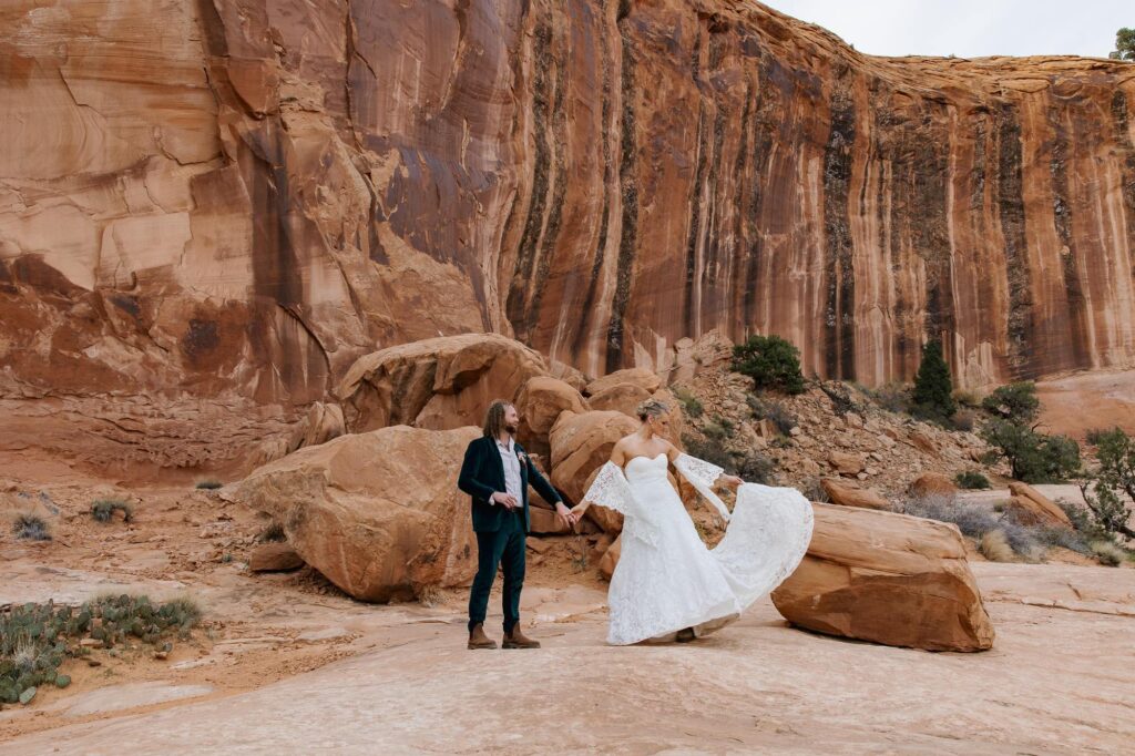 A groom twirls his bride in front of a backdrop of Red Rocks in Utah
