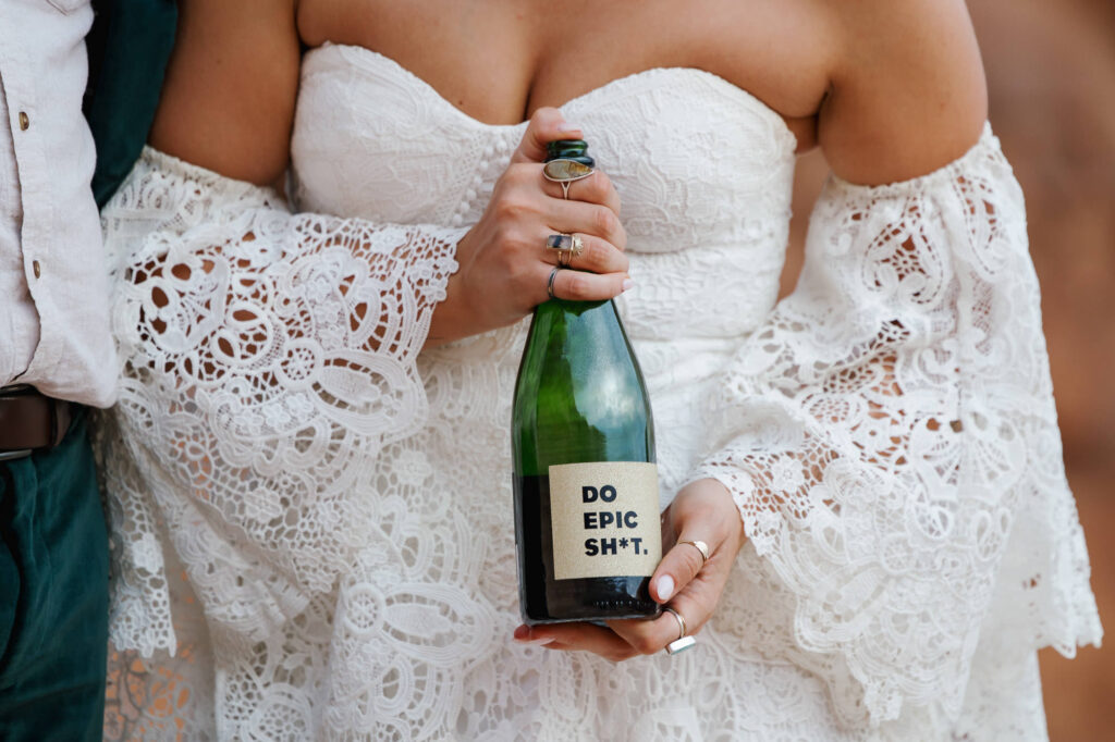 A bride holds a bottle of champagne that is called " do epic shit"
