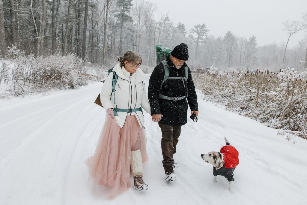 A bride, groom, and their dog walk in the snow during their adventure elopement