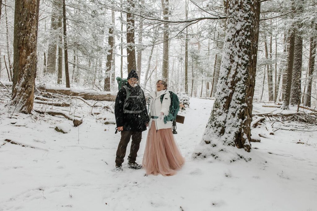 A bride and groom stop to enjoy the snow on the trail as they hike towards their ceremony location
