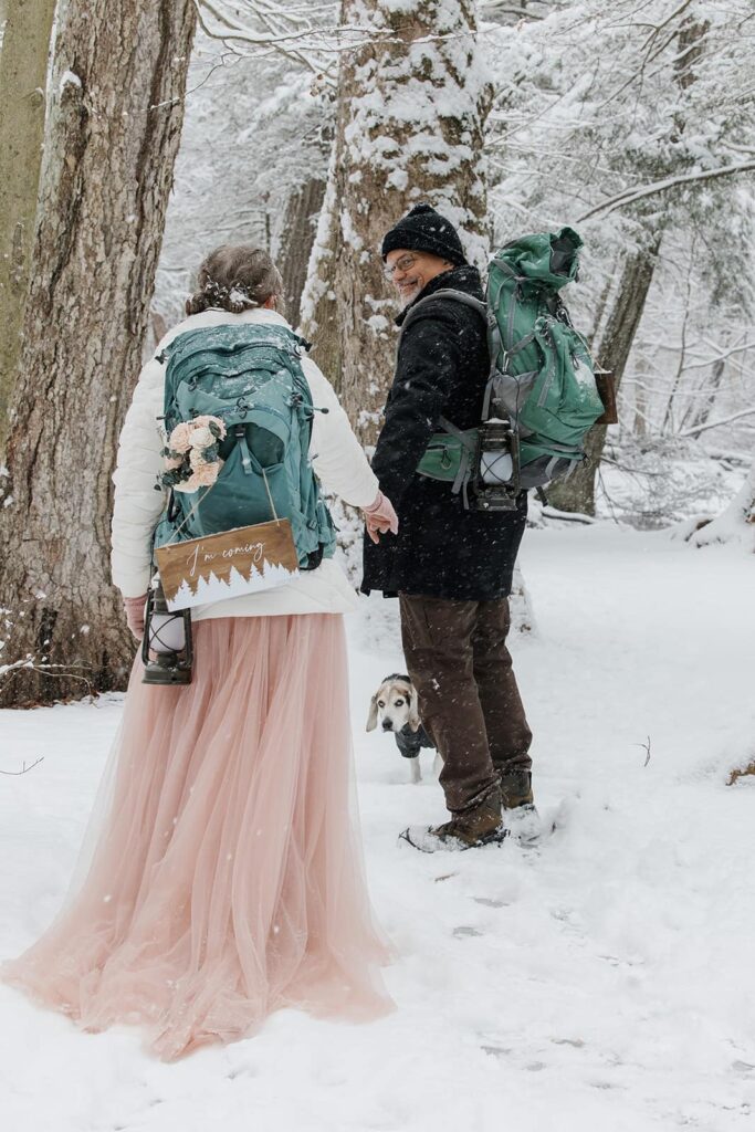 A groom looks back at his bride as they hike on the trail in the snow during their elopement