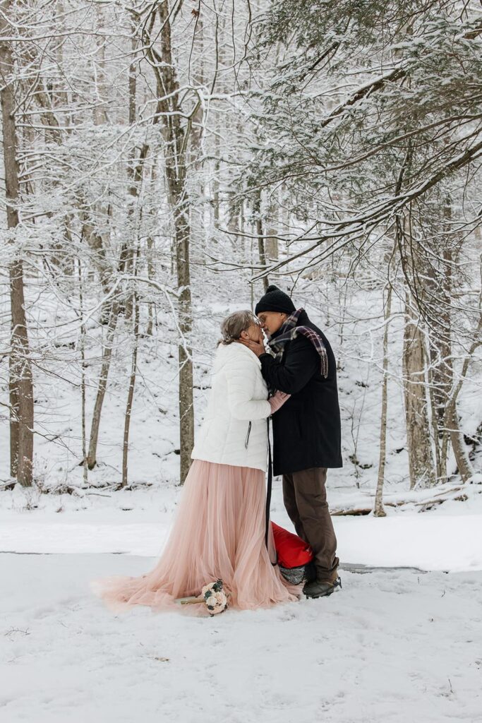 A bride and groom share their first kiss during their snowy elopement ceremony at Ricketts Glen State Park
