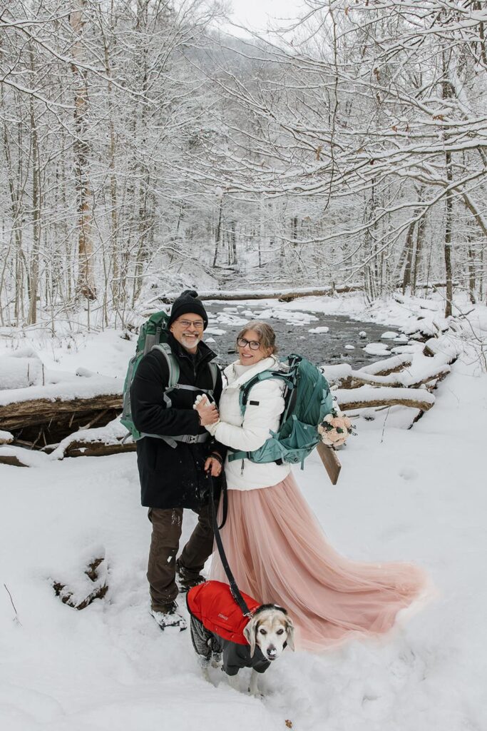 A bride, groom, and their dog stand in front of Kitchen Creek on their elopement day at Ricketts Glen.