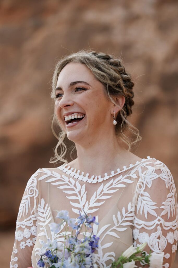 A bride laughs while she is getting ready on her elopement day.She is wearing a Boho see through lace dress