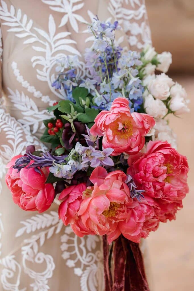 A bride holds a  big colorful bouquet of flowers on her elopement day. The bouquet is full of pinks, blues and whites, and has a velvet ribbon