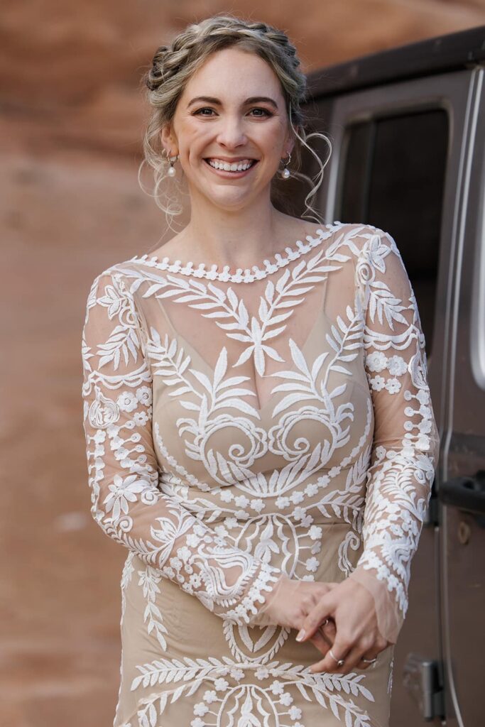 A birde in a boho see through lace dress smiles as she stands next to her jeep. She looks excited for her first look with her husband to be. 