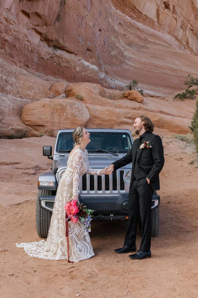 A bride and groom hold hands and share a laugh and excitement as they see one another for the first time during their elopement in the desertof Utah. 