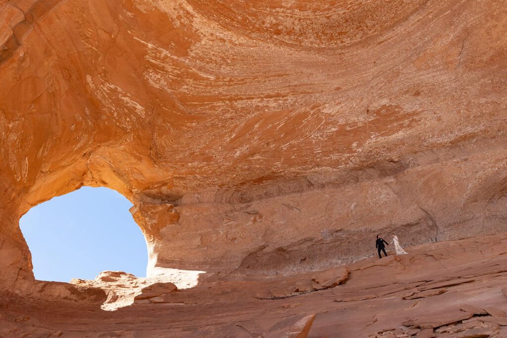 A bride and groom walking towards the center of Looking Glass Arch on their elopement day in Moab