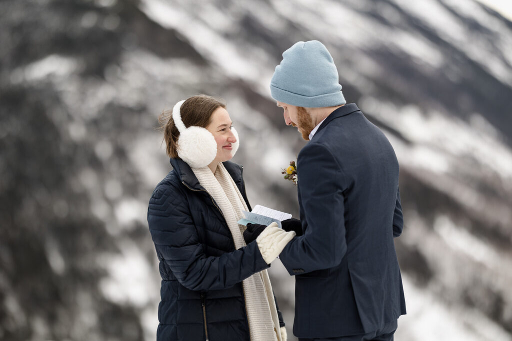A bride holds her grooms hands as he says his vows during their chilly snowy elopement in the White Mountains
