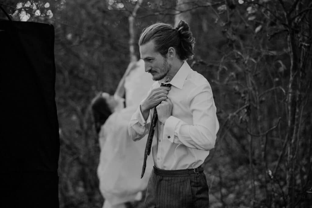 A groom tightens his tie as he gets ready for his sunrise elopement at Stony Man Summit